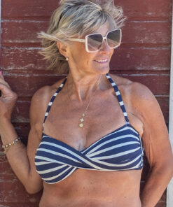 eldre kvinne på stranden iført bikini med blå og hvite striper fra merket salta bad